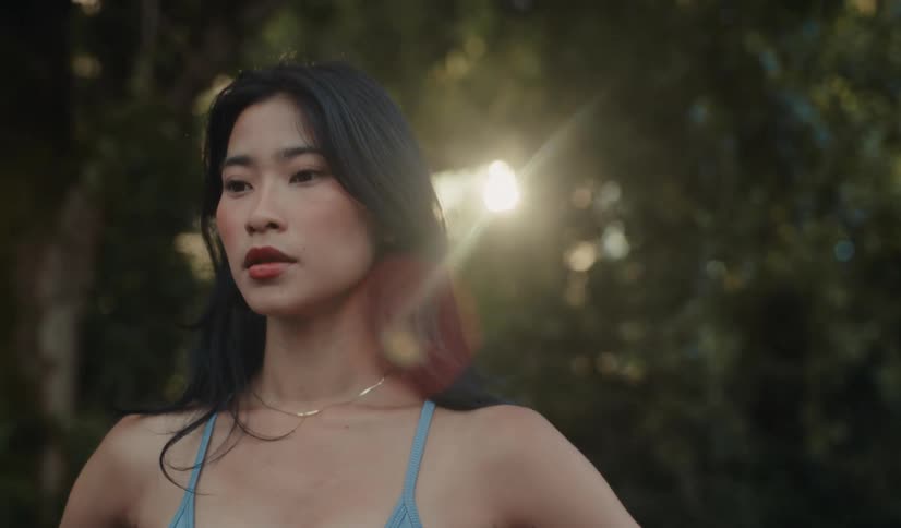 An athletic Asian woman catches her breath in a sun-drenched forest in slow motion after her workout