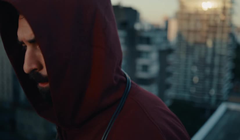 Slow motion close-up of a determined man in a red hoodie jumping rope on a city rooftop at dawn