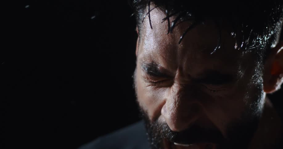 Dramatic slow-motion close up of a bearded man screaming with intense emotion as water splashes around him
