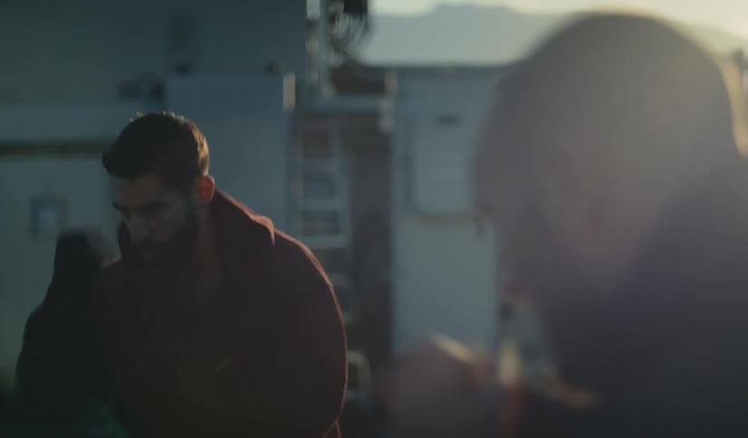 Over the shoulder slow-motion shot of two men shadowboxing on a rooftop at dawn, ending their session with a friendly hug