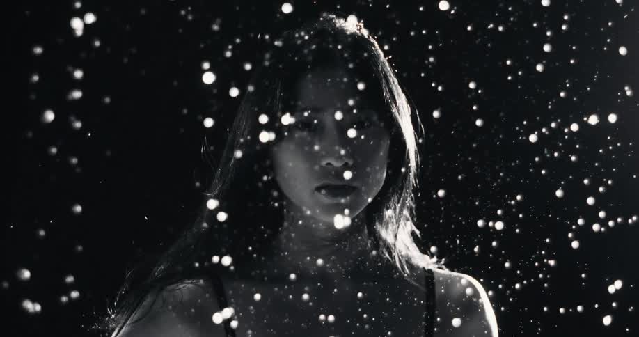 Artistic black and white cinemagraph of a mysterious woman's portrait with illuminated particles falling around her in slow motion