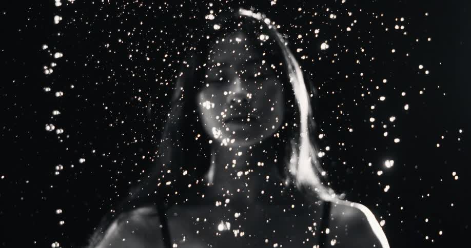 Black and white slow motion cinemagraph of shimmering water drops falling in front of a woman's out-of-focus silhouette