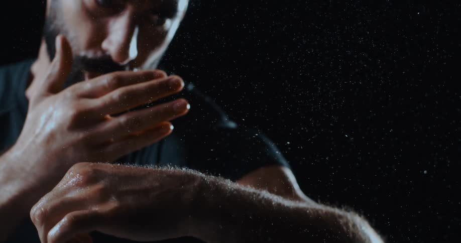 Dramatic slow motion close-up of an intense man standing in the rain against a dark background
