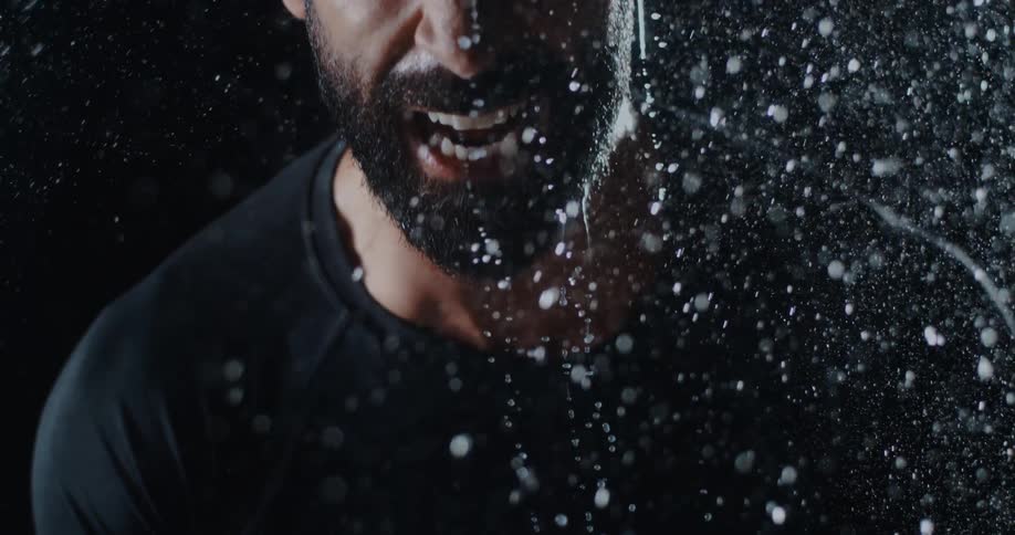 Slow motion close-up of an intense man screaming in the rain, with the camera tilting down his face