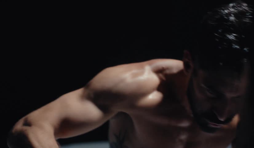 High angle slow motion view of a shirtless, determined boxer throwing punches in a dark, dramatically lit room