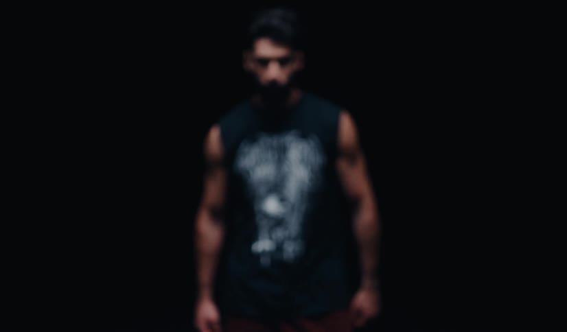 An intense, bearded man slowly walks out of the shadows, staring directly into the camera with a determined look