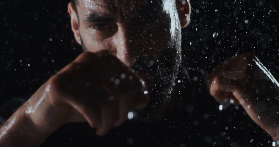 A powerful bearded boxer trains in the rain, throwing a punch directly at the camera in dramatic super slow motion