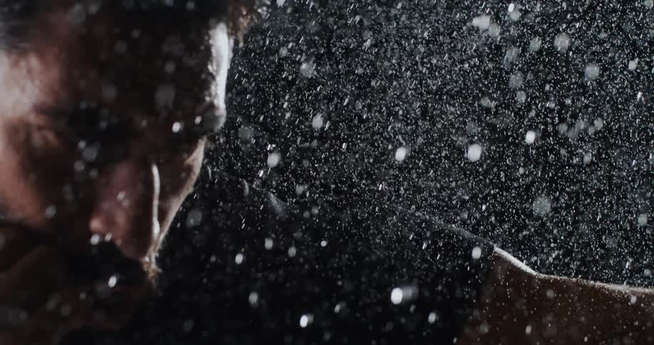 A determined male boxer trains intensely in the pouring rain, captured in a dramatic slow-motion close-up