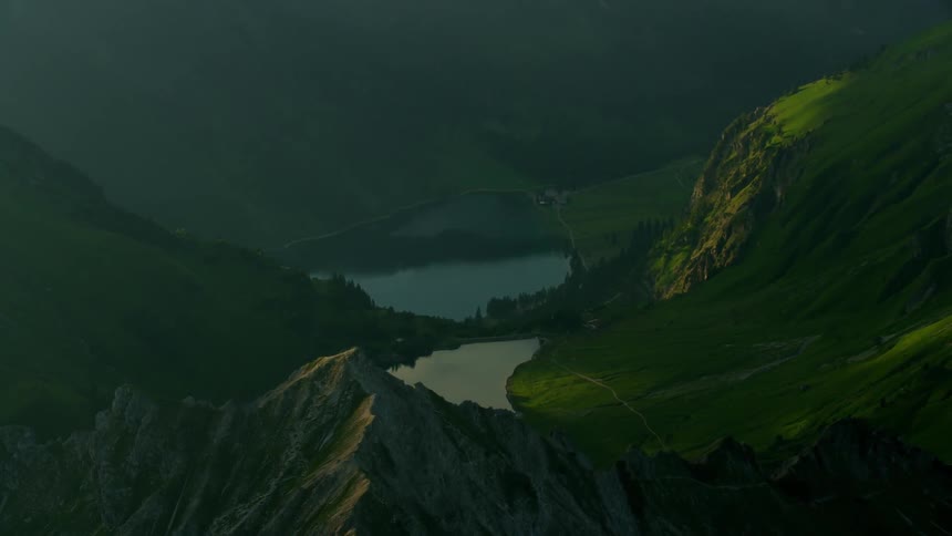 A cabin sits lakeside in a mountainous region