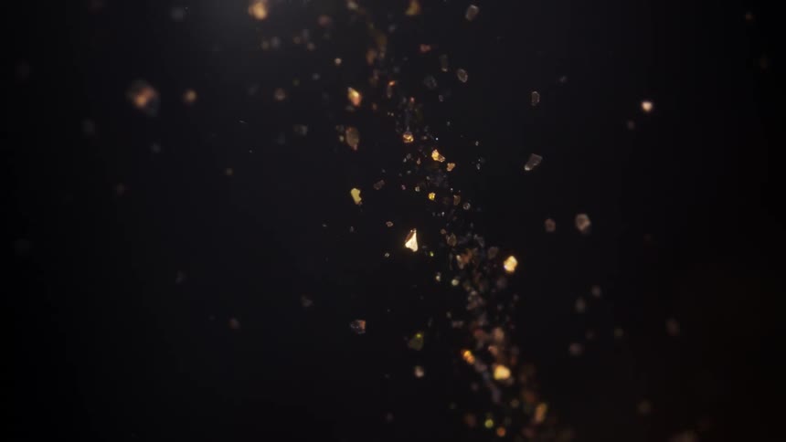 A magical stream of shimmering gold particles and embers floats slowly against a black background