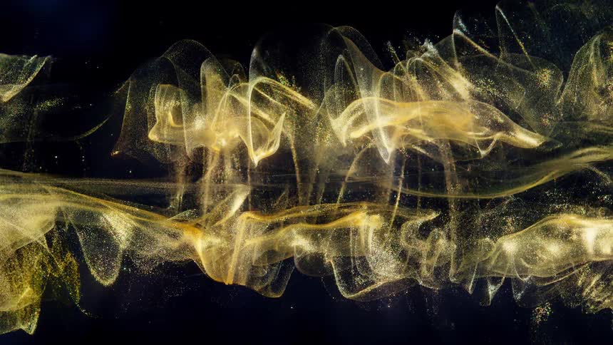 A mesmerizing cloud of golden glitter particles swirls elegantly through dark liquid, creating a luxurious abstract background