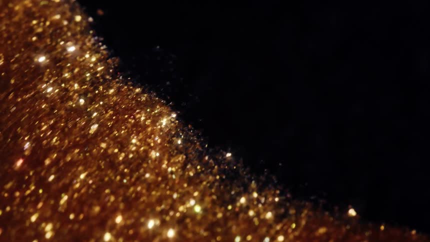 A wave of darkness slowly covers a field of shimmering golden glitter in this elegant macro shot