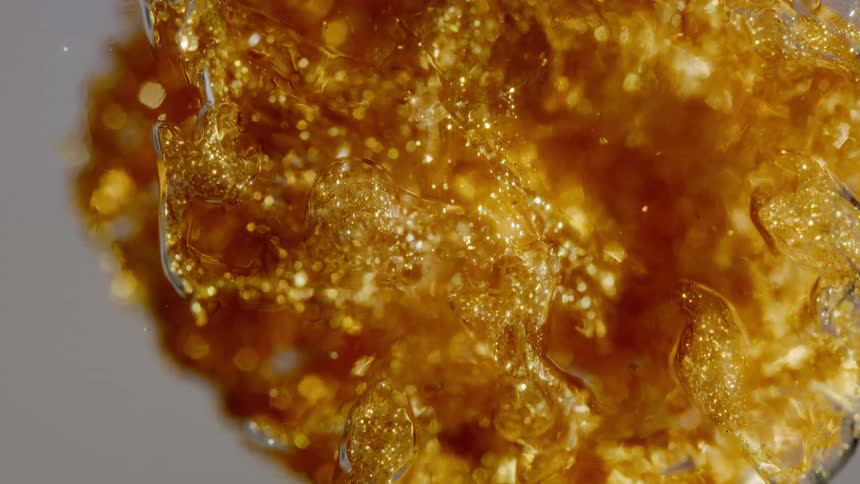 A mesmerizing macro shot of sparkling gold glitter slowly moving and crystallizing in a viscous amber liquid