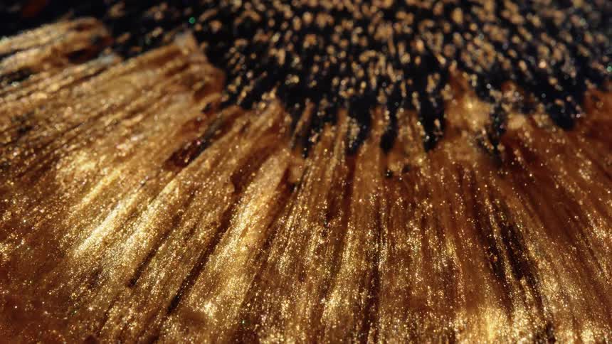 Shimmering liquid gold flows and expands in a mesmerizing abstract macro shot