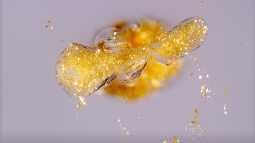An abstract macro shot of shimmering gold glitter suspended and moving slowly in a clear fluid against a white background