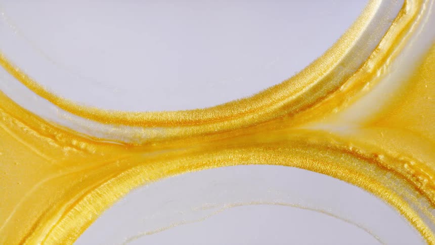 Shimmering gold liquid pulls apart in slow motion, creating an abstract hourglass shape on a white background