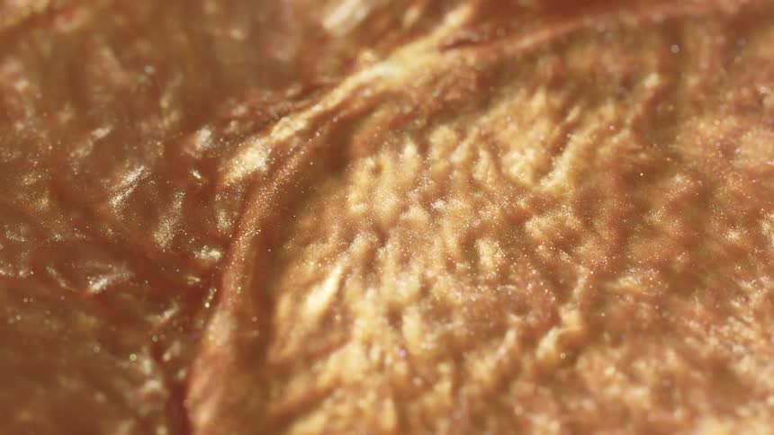 A mesmerizing macro shot of a slowly moving, textured golden liquid shimmering with light