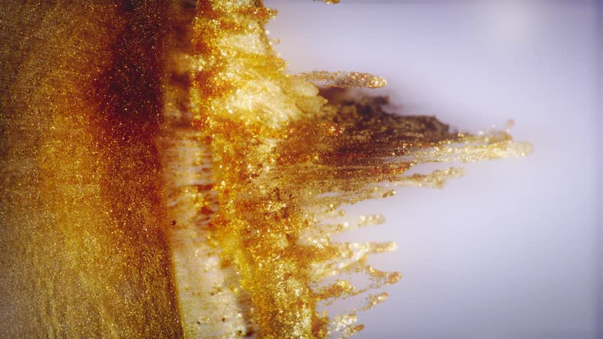 A vertical macro shot of shimmering golden paint spreading out like intricate fractals against a clean white background