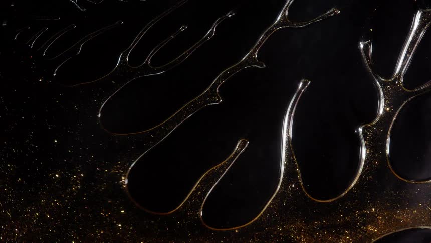 Molten gold with shimmering particles flows and then vanishes into a cloud of sparkling dust on a black background