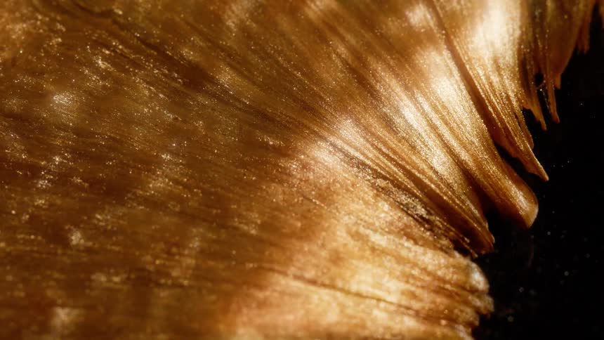Shimmering golden metallic liquid with sparkling glitter particles creates a luxurious and abstract texture on a black background