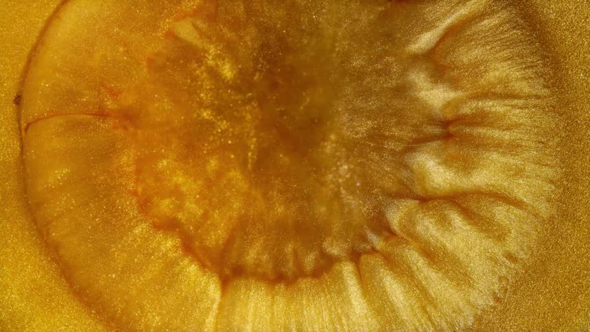 A mesmerizing macro shot of shimmering gold liquid glitter paint expanding and flowing in an abstract pattern