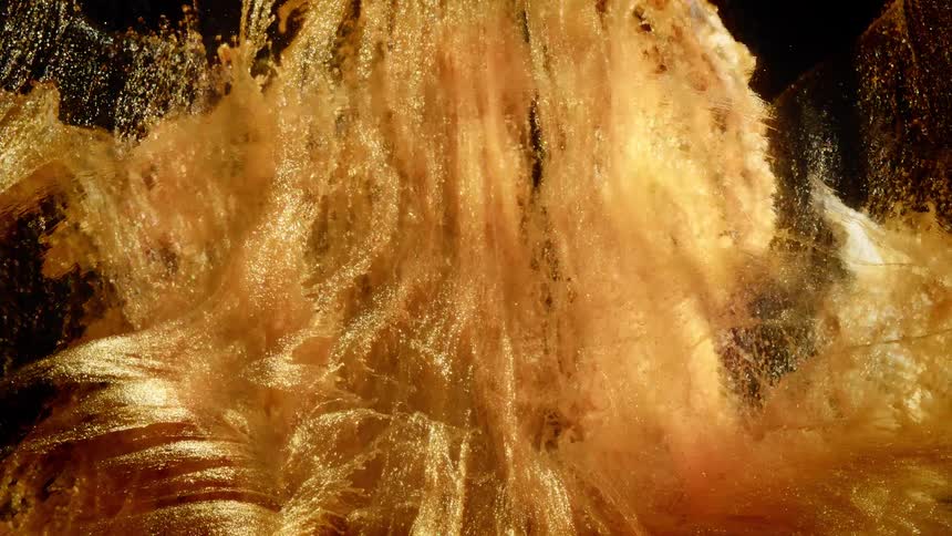 A mesmerizing cascade of sparkling golden liquid creates an abstract, flowing spectacle against a dark background