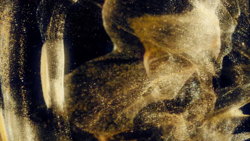 A mesmerizing cloud of golden glitter swirls slowly in dark liquid, creating a luxurious and abstract background
