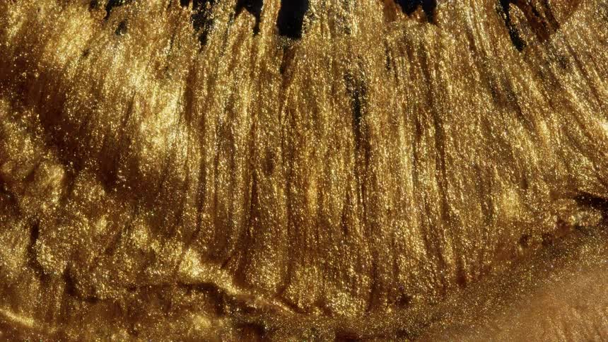 An abstract macro view of a thick, sparkling golden liquid flowing downwards in slow, mesmerizing waves