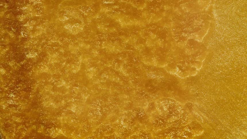 Overhead shot of a thick, shimmering golden liquid with glitter flowing in slow motion, creating a mesmerizing abstract background