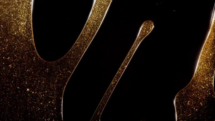 Glistening gold glitter suspended in a clear, viscous liquid slowly drips down a black surface in a mesmerizing macro shot