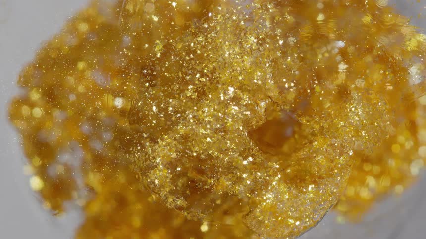 A mesmerizing macro shot shows golden glitter particles swirling in a vortex within a clear liquid