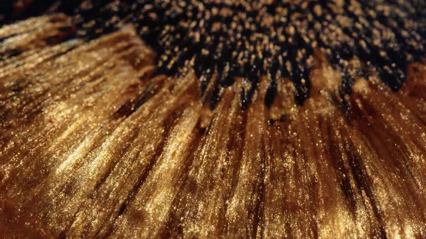 A mesmerizing macro shot of golden glitter paint flowing over a black background, creating an abstract and luxurious visual