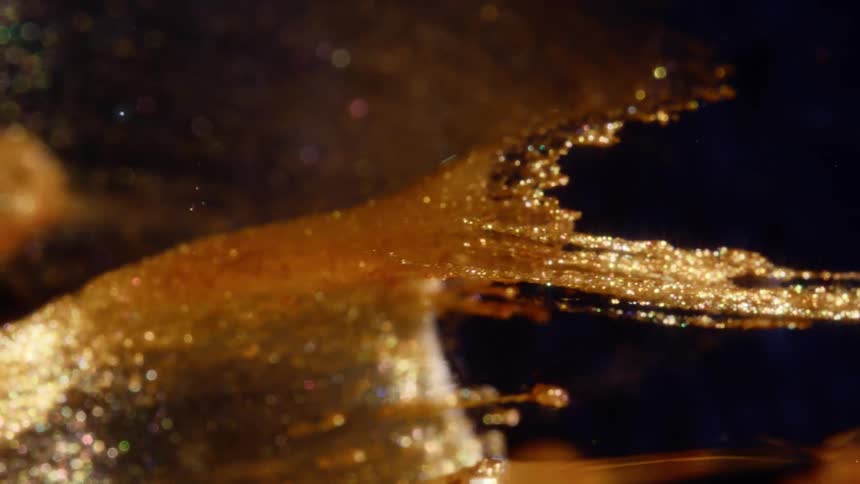 A mesmerizing macro shot of sparkling gold glitter slowly stretching and flowing in dark liquid