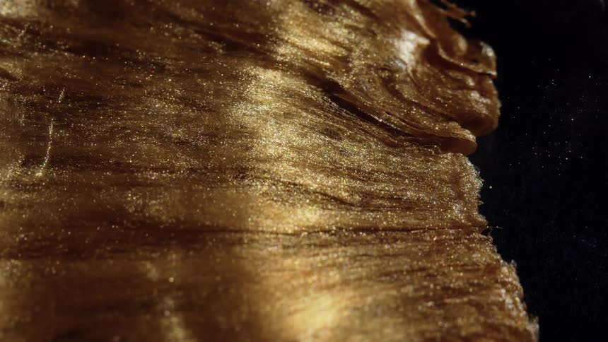 An abstract macro shot of a viscous golden substance with shimmering glitter particles