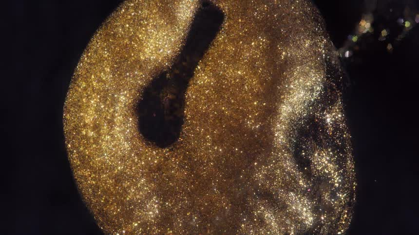 An abstract macro shot of shimmering golden particles slowly swirling in a cosmic dance against a dark background