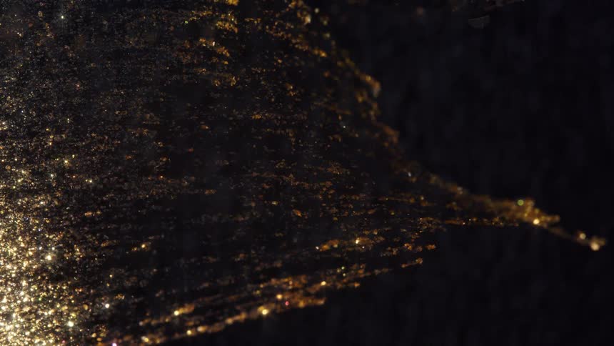 Shimmering gold particles slowly flow like a river through a dark fluid background