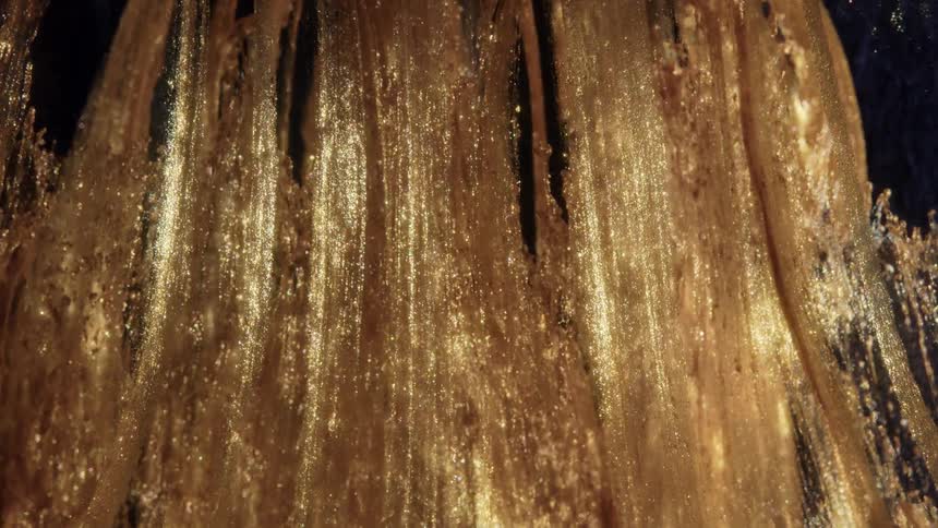 A macro shot of thick, glittering gold paint slowly dripping downwards in a mesmerizing abstract flow