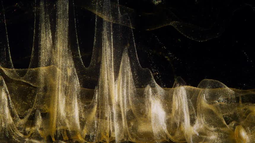 Slow-motion abstract shot of golden glitter particles creating ethereal, undulating forms in a dark liquid
