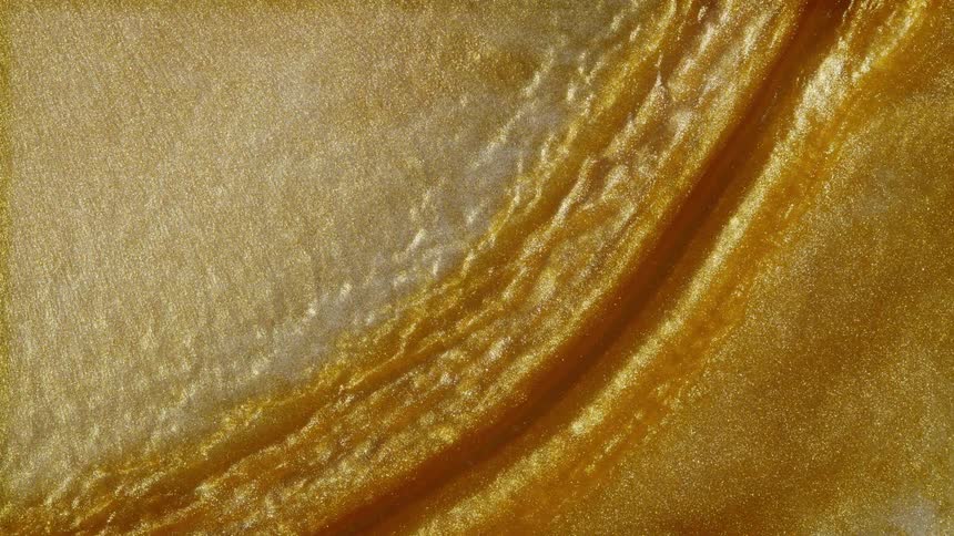 A shimmering river of golden metallic paint flows and ripples in slow motion