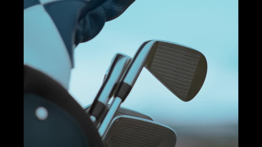 A golfer's gloved hand carefully selects an iron from a golf bag in a slow-motion close-up
