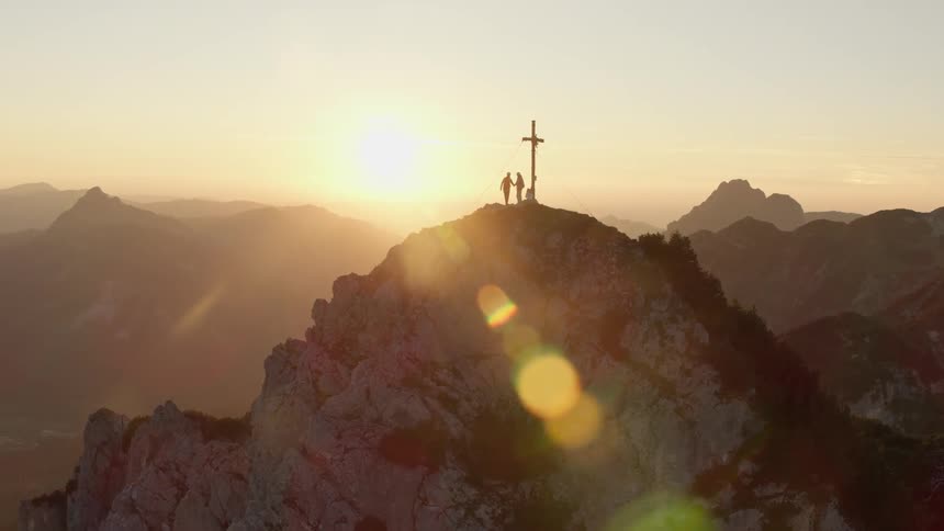 Climbers stand next to a cross on a mountain peak