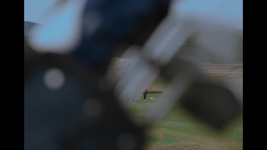 A creative perspective from behind a golf bag frames distant golfers as one takes a swing on a beautiful green course