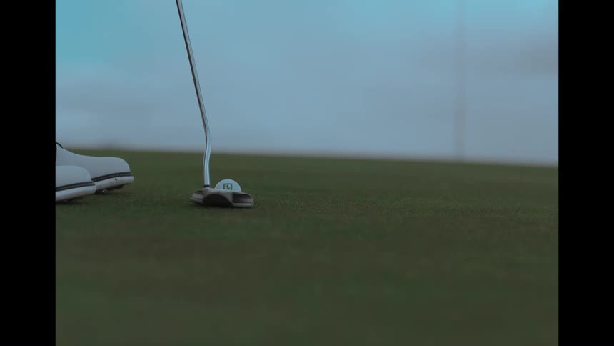 A golfer carefully lines up and putts a golf ball on the green in a slow-motion close-up