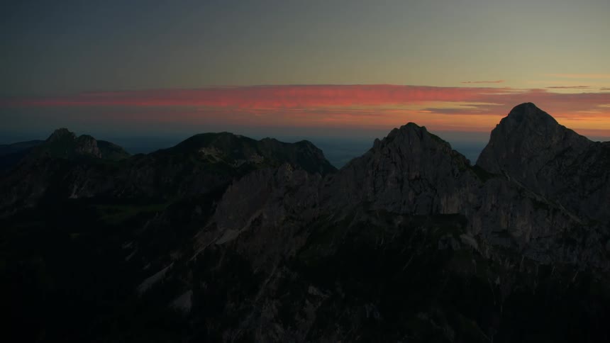 The tall mountains have red tinged clouds from the setting sun