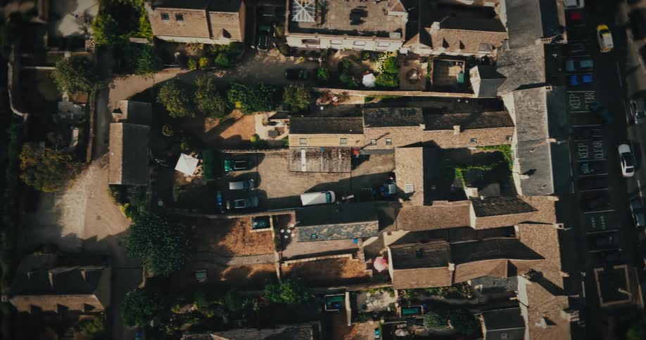 An aerial top-down view slowly zooms out over the rooftops of a historic village in the English countryside