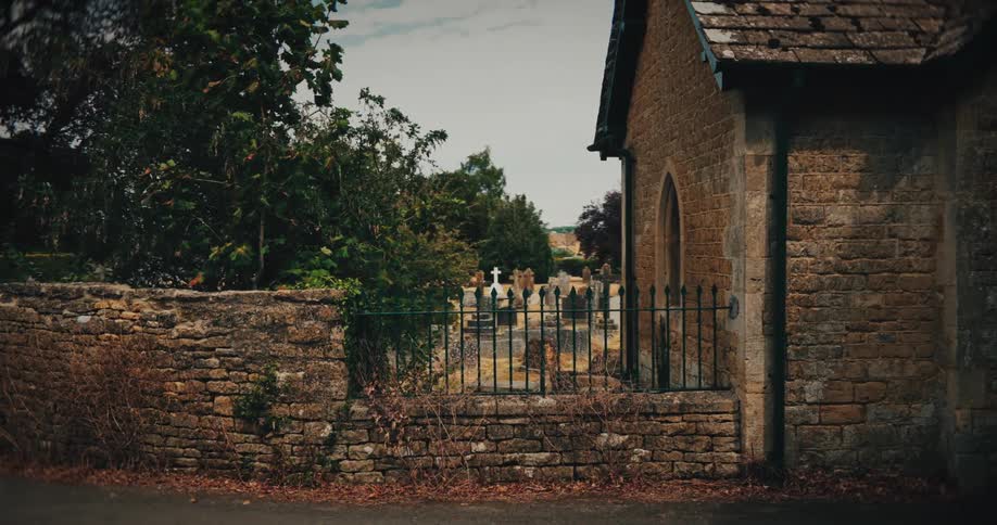 A slow dolly shot reveals an ancient stone church and a quiet, weathered graveyard behind a low stone wall