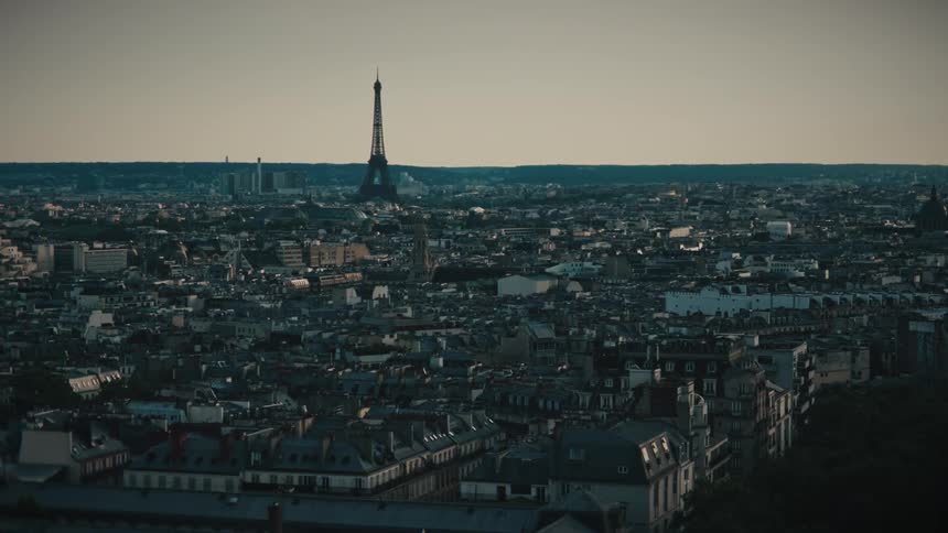 A slow aerial pullback shot reveals the vast cityscape of Paris with the Eiffel Tower standing tall on the horizon during a hazy sunset