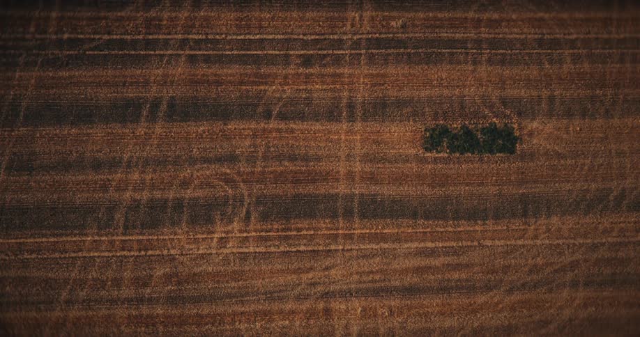 An abstract aerial shot spins and zooms in on the textured patterns of a brown field