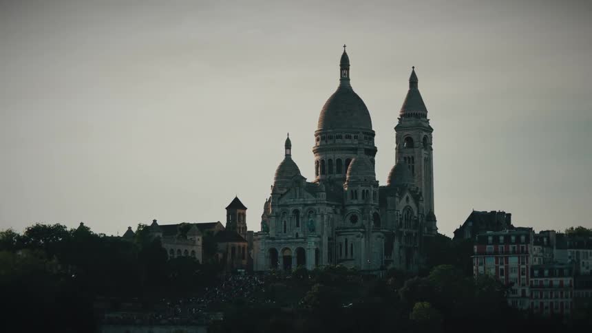 A slow zoom out reveals the majestic Sacré-Cœur Basilica on Montmartre hill against the hazy sunset sky in Paris, France