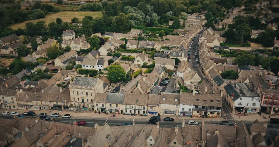 A static aerial cinemagraph captures the timeless beauty of a quaint English village with its historic stone buildings and surrounding green countryside